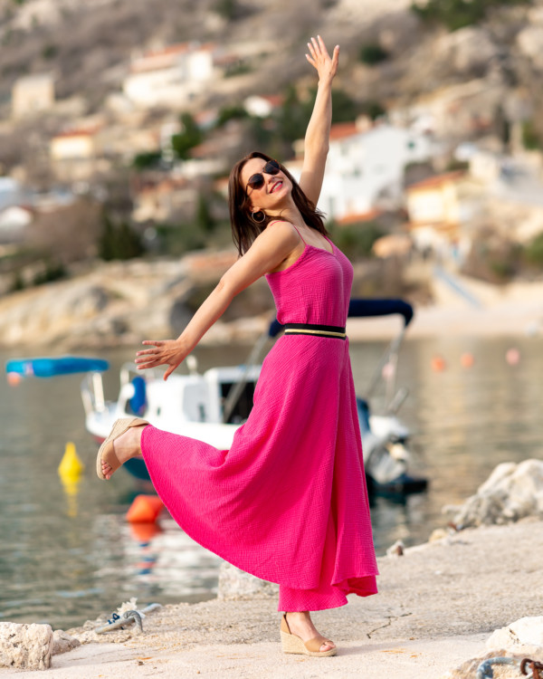 žena v mušelínovom oblečení magentovej farby kráča pri mori