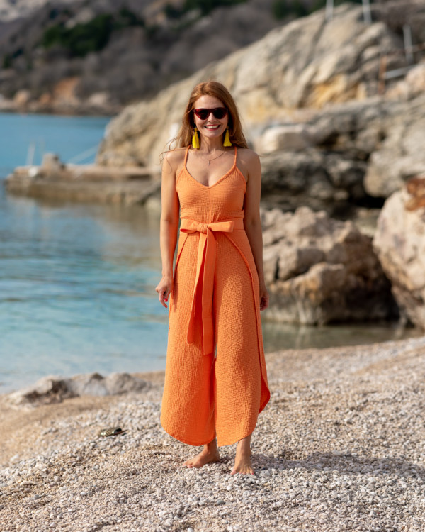 Žena v oranžovom mušelínovom oblečení značky Love Colors kráča pri mori