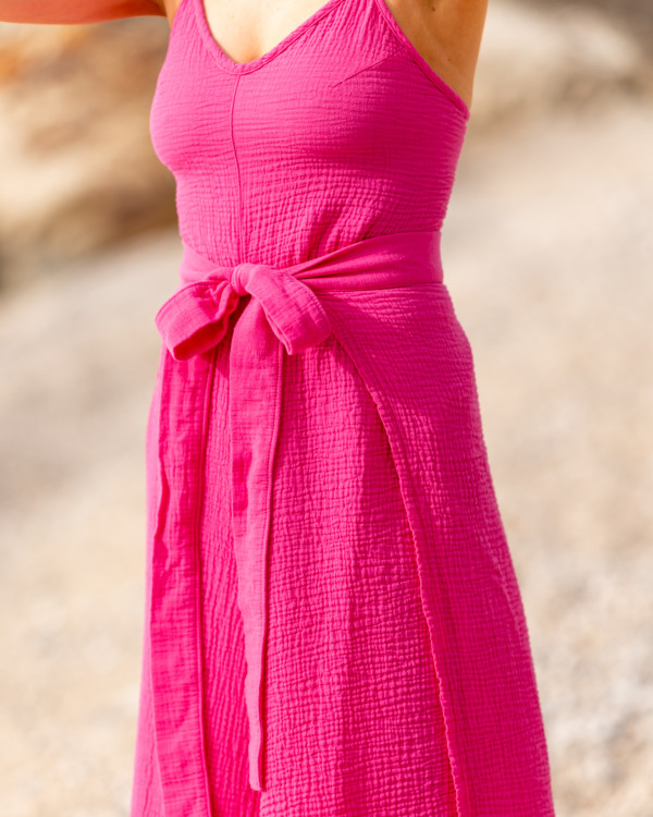 Žena v magentovom mušelínovom oblečení značky Love Colors kráča pri mori